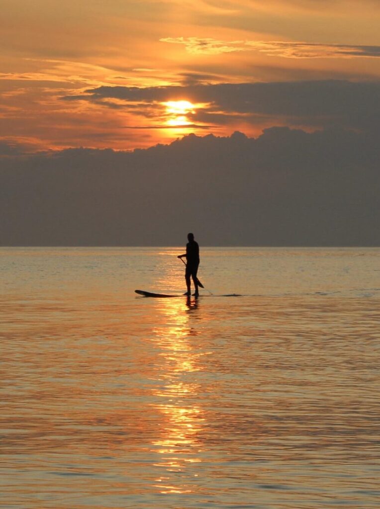 person auf einem SUP auf der Nordsee und im Hintergrund der Sonnenuntergang